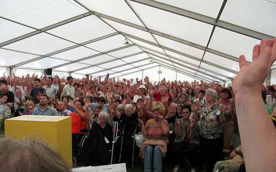 Cientos de personas con las manos levantadas durante una asamblea de oración de la Renovación Carismática, dentro de una carpa.
