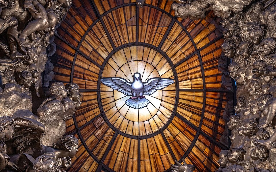 Vitral dorado con una paloma blanca en el centro, rodeado de esculturas de ángeles y nubes de bronce.