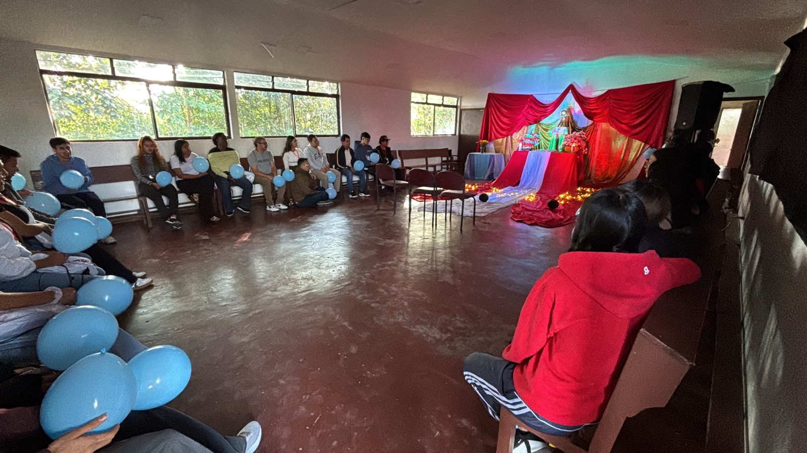 Jóvenes sentados en círculo con globos azules frente a un altar con telas rojas y velas, durante el Seminario de Vida Nueva en el Espíritu.